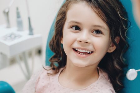 Curly haired little girl looking and smiling to the dentist after a checking up