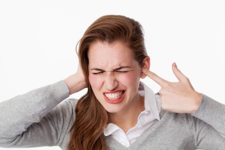 tinnitus concept - enraged young woman having painful headache,covering closed ears,annoyed by loud noise not wanting to hear their side of story