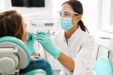 European mid pleased dentist woman in face mask working in dental clinic