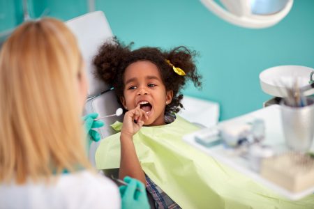 Little child in dental chair show with finger tooth for repairing