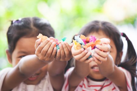 Two asian child girls holding sweet candies in thier hands and share to each other